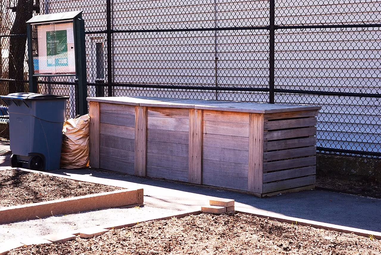 Wooden compost bins with three compartments in a garden.